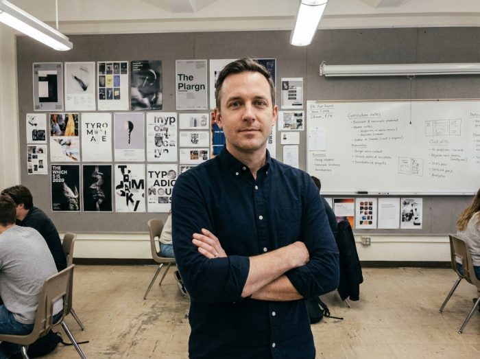 Enseignant en design graphique devant un mur de critique couvert de projets d'étudiants dans une école spécialisée